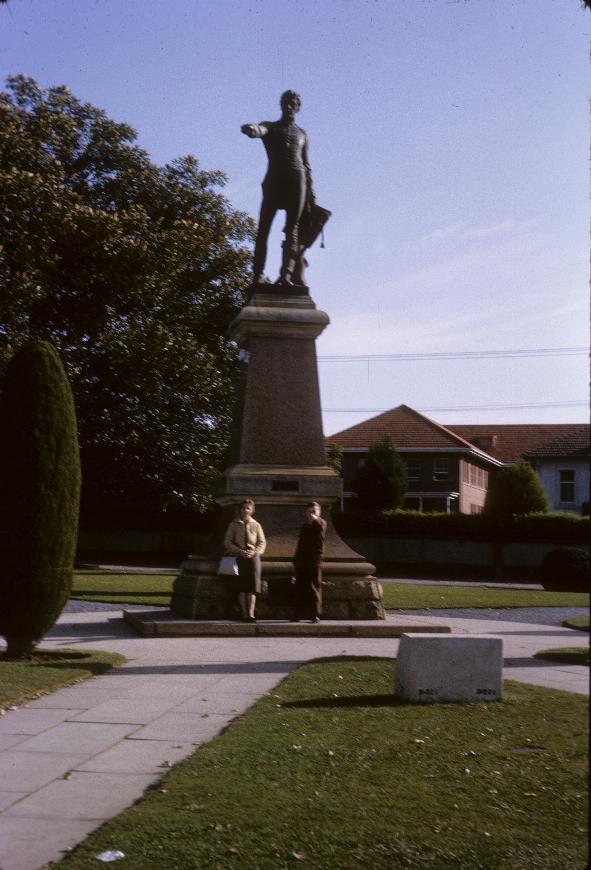 Statue of man pointing with right hand; mother and son at the base