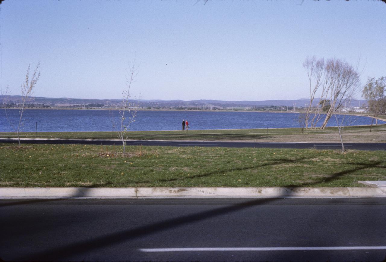 Two people standing on edge of lake; distant trees and hills