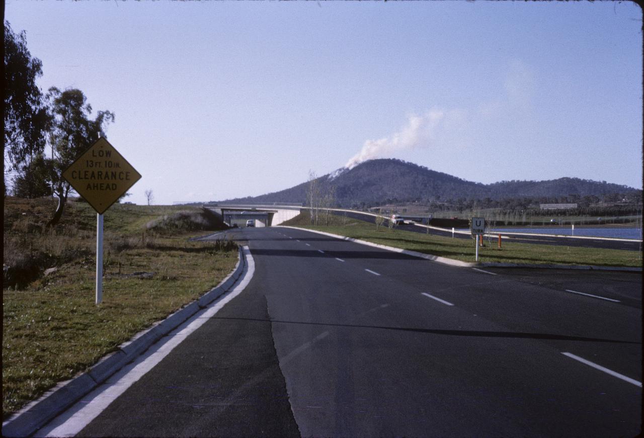 Overpass and bridge across lake, mountain with fire on one side in the distance