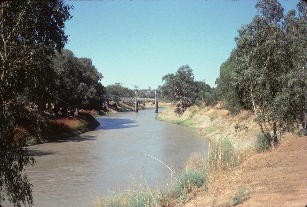 Brown river, trees along bank and iron bridge