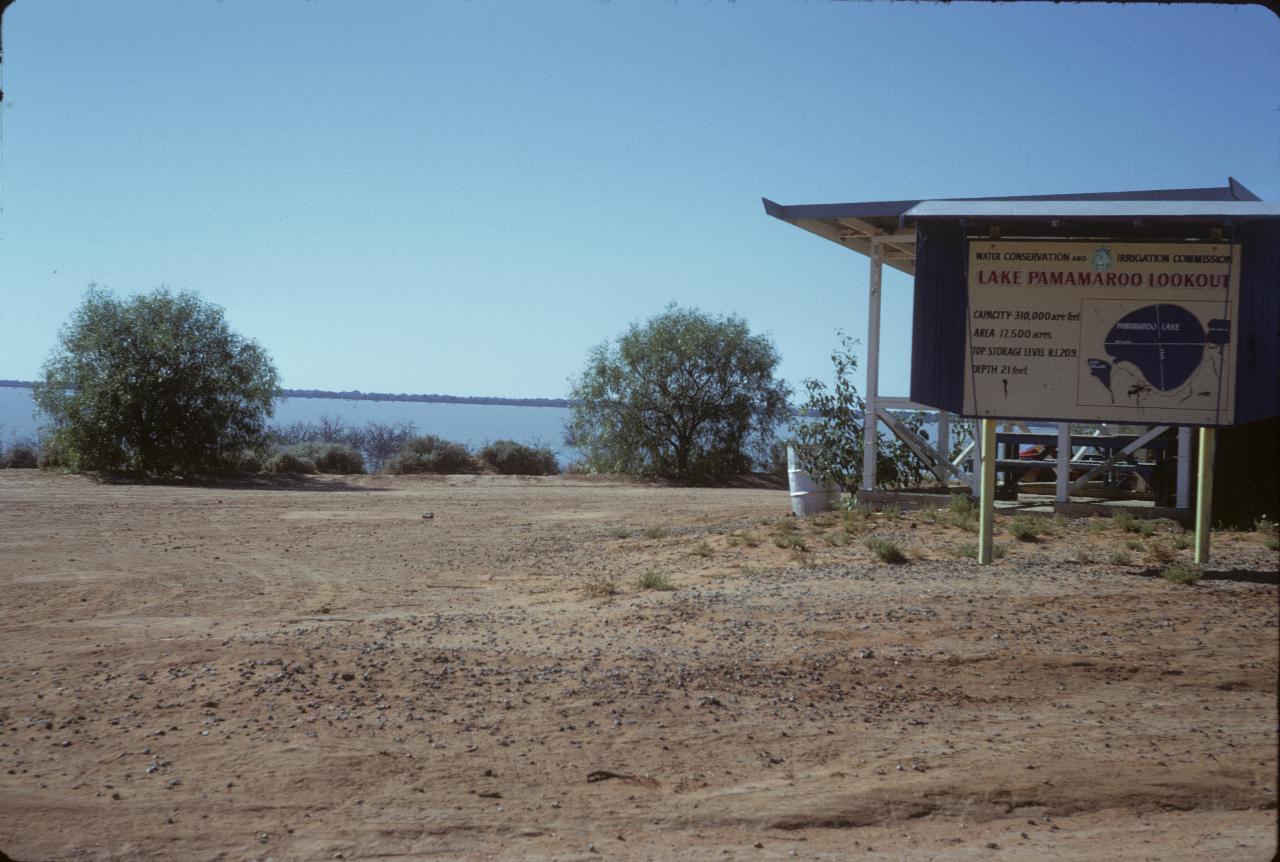 Sandy shore, with display board and lake in the rear
