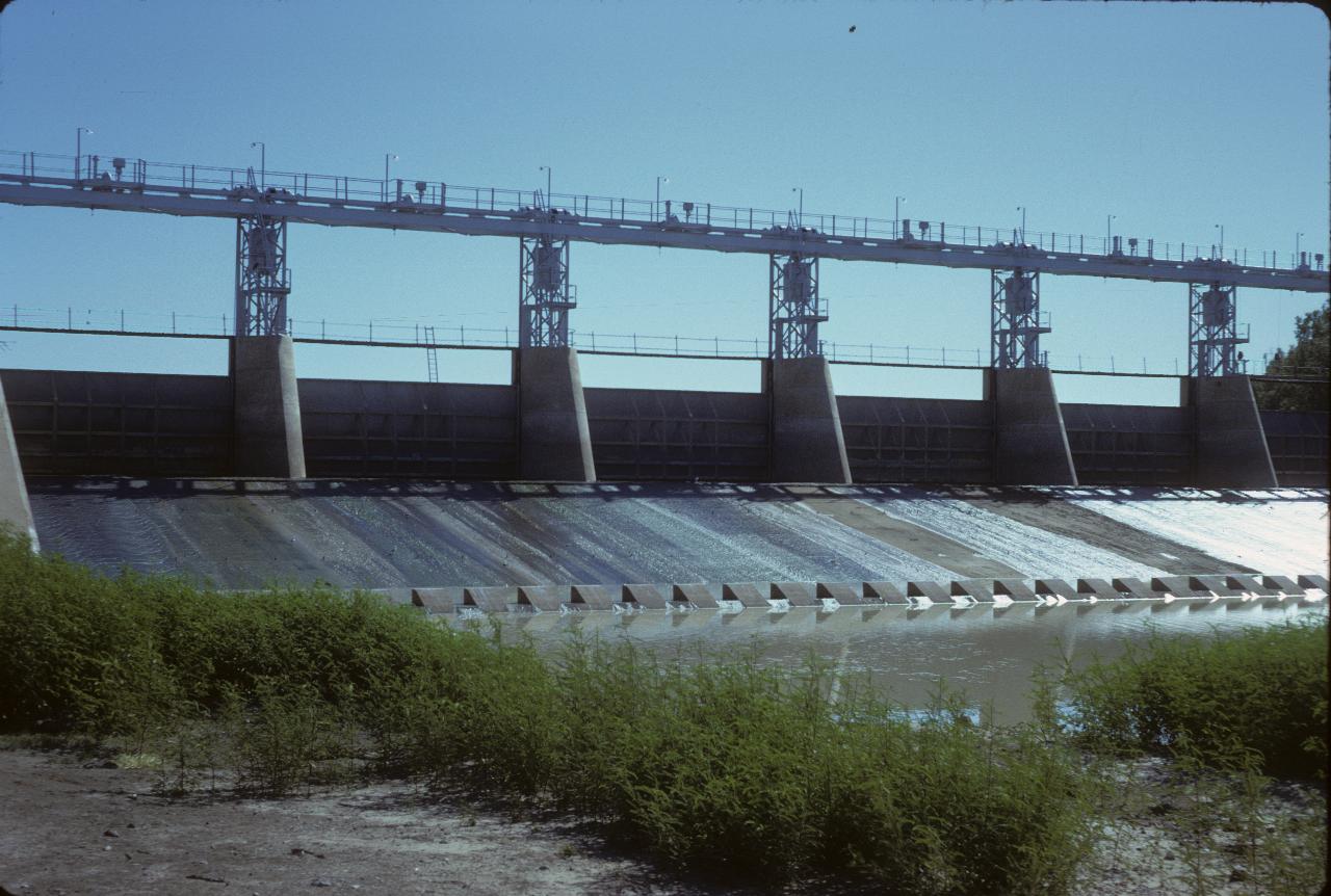 Low concrete dam wall with 6 lift gates, seen from downstream; no water coming out