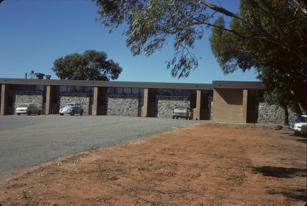 Bare ground, ashphalt  parking area and flat roof building with stone walls