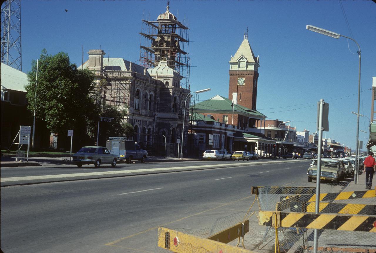 Wide street with grand stone building with scaffolding and another building with solid tower and clock