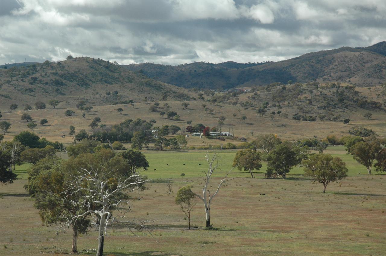 View over green or brown pasture, river not really visible, to farmstead and distant hills