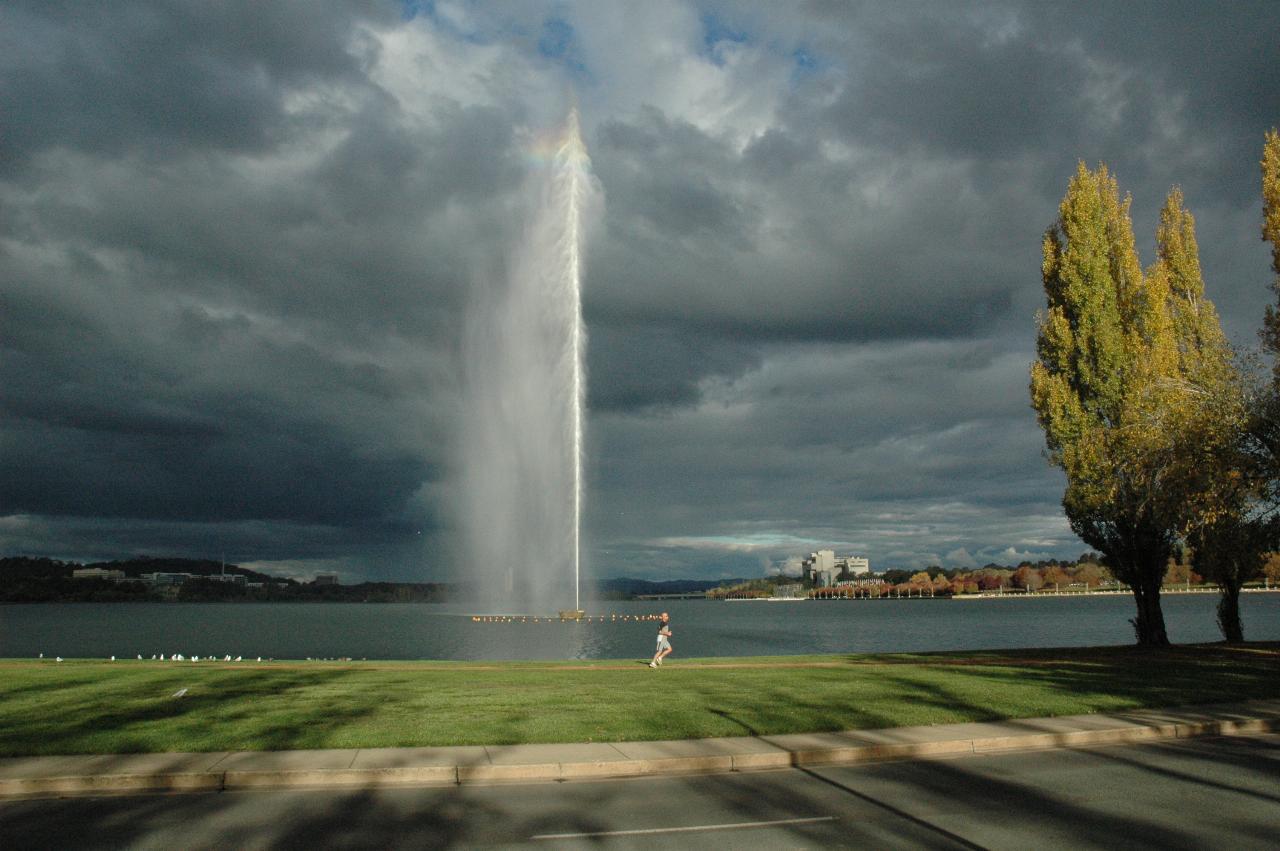 Dark background, 200m high water jet in sunshine, jogger running past